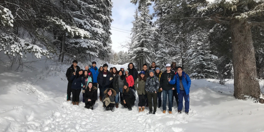A big group of students poses in a snowy forest.