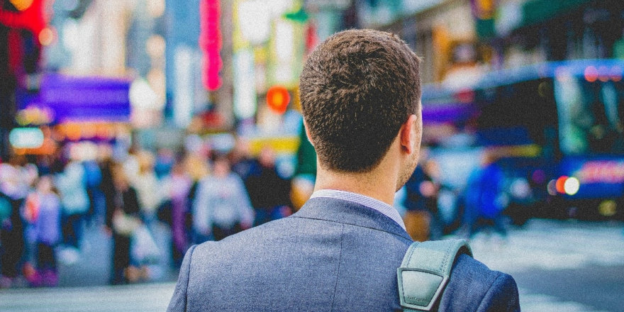 A young man in business attire looks out across a busy city street.
