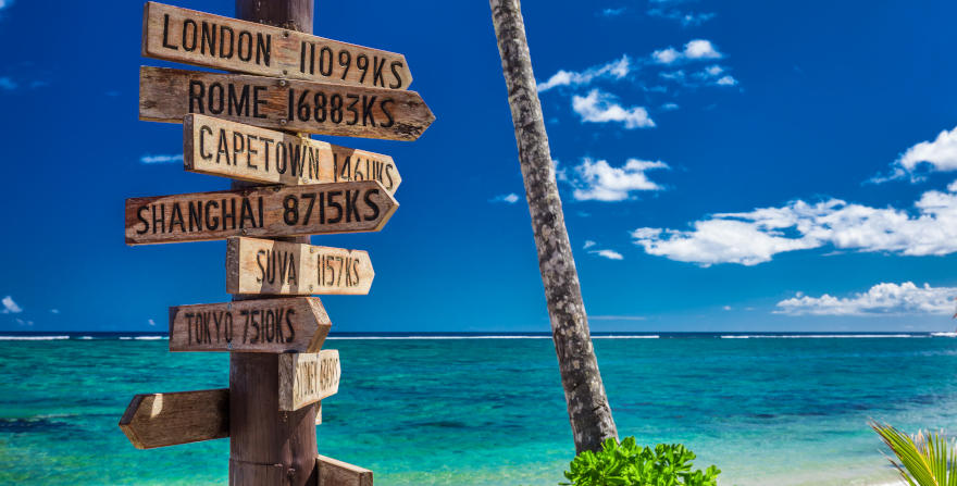 A street sign in a tropical location, showing the direction and distance to many popular destinations worldwide.