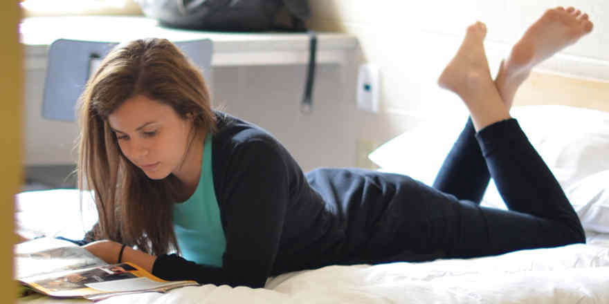 A young woman lies on a bed, studying.