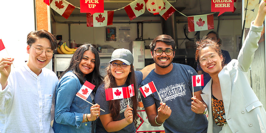 A group of cheerful international students waves Canadian flags at Conestoga College.