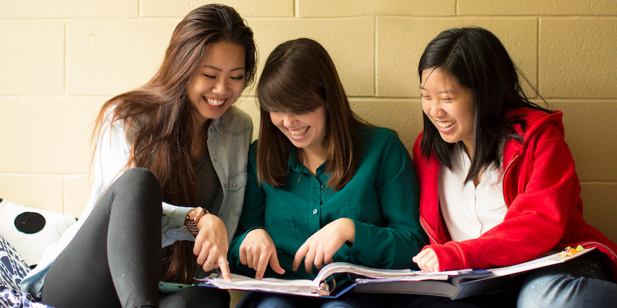 Three students laugh over a binder, making the most of their last year of high school.
